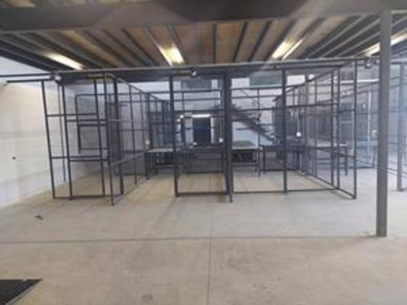 Industrial utility space featuring concrete flooring, exposed steel ceiling beams, and modular metal partitioning suitable for storage or workshop use.