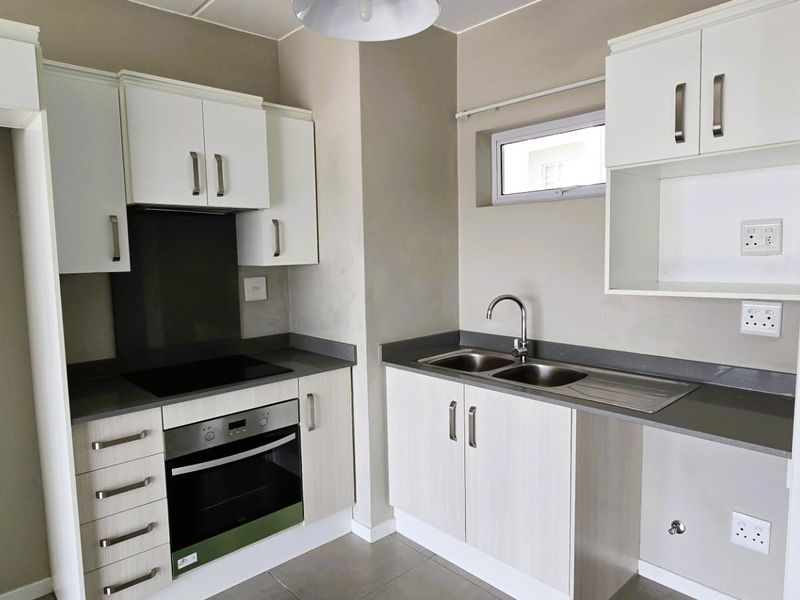Modern kitchen featuring white cabinetry, stone countertops, built-in oven, electric hob, and a double bowl stainless steel sink.