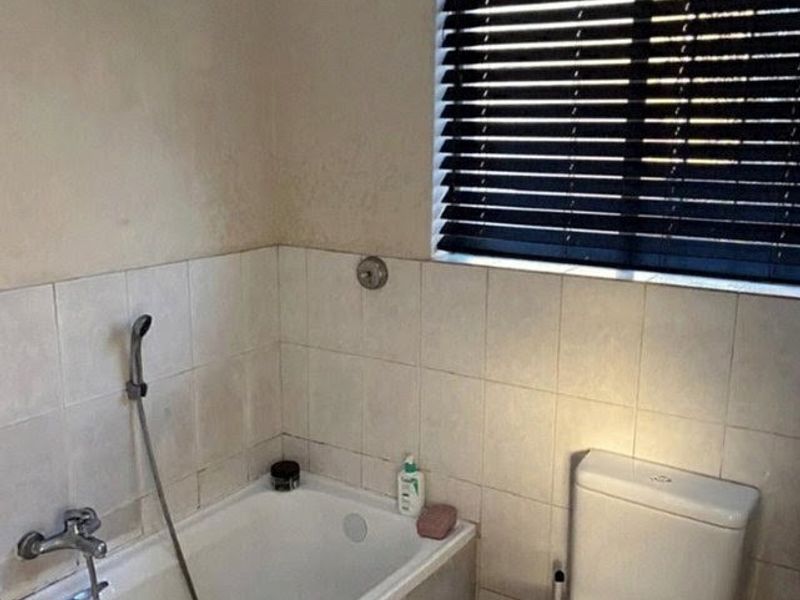 A functional bathroom featuring a bathtub with a handheld shower attachment, a standard toilet, and tiled wall finishes with window blinds.