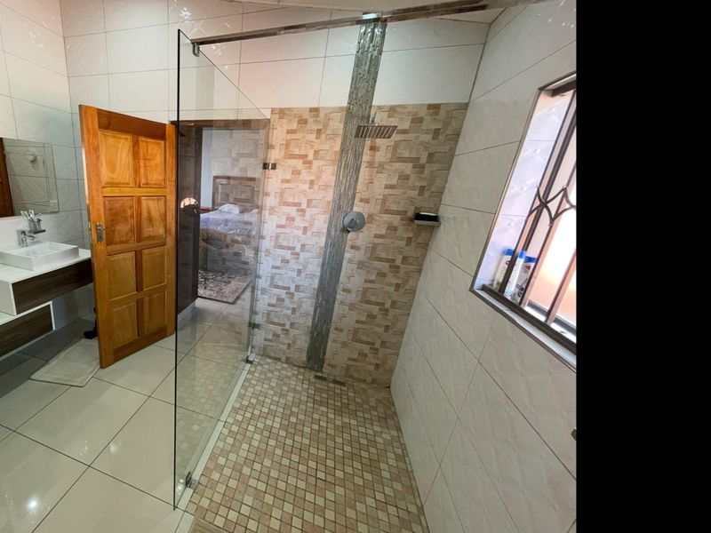 Modern bathroom featuring a spacious walk-in shower with glass screen, wall-mounted vanity with vessel sink, and neutral tiled finishes throughout.
