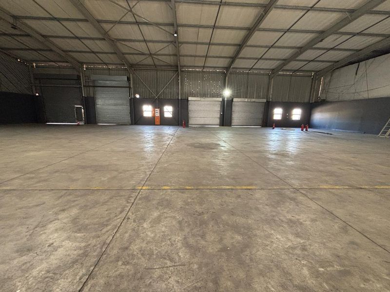Spacious industrial warehouse featuring high ceilings, concrete flooring, and multiple roller shutter doors, providing excellent access and versatile storage or manufacturing space.