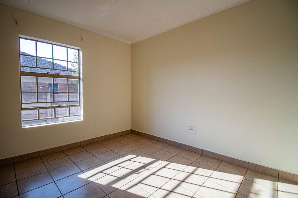 A bright, empty bedroom featuring neutral wall paint, tiled flooring, and a large window providing natural light.