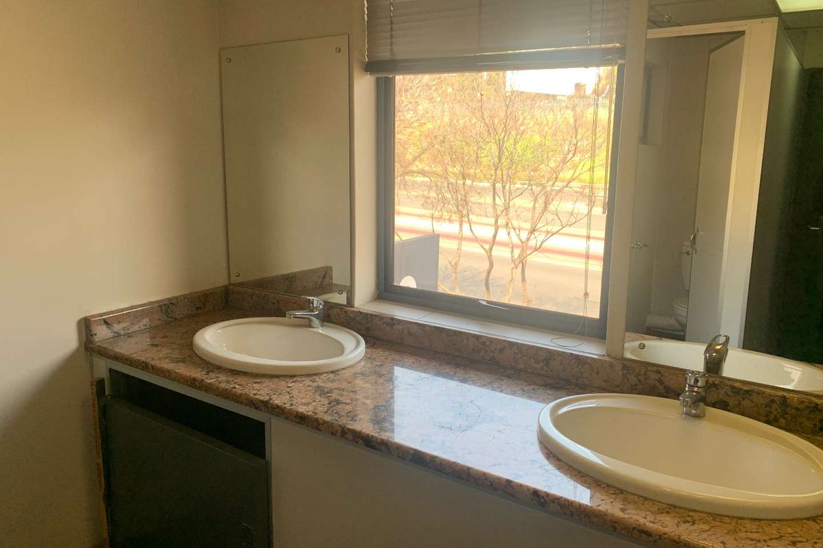 Office bathroom featuring a dual-basin vanity with granite countertop, integrated sinks, and wall-mounted mirrors.