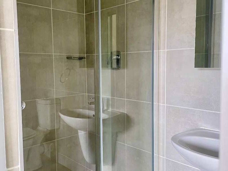 A clean, modern bathroom featuring a glass-enclosed shower, pedestal sink, and neutral ceramic wall tiling.