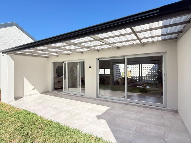 A modern covered patio featuring large format floor tiles, a translucent roof structure, and wide sliding glass doors providing seamless indoor-outdoor flow.