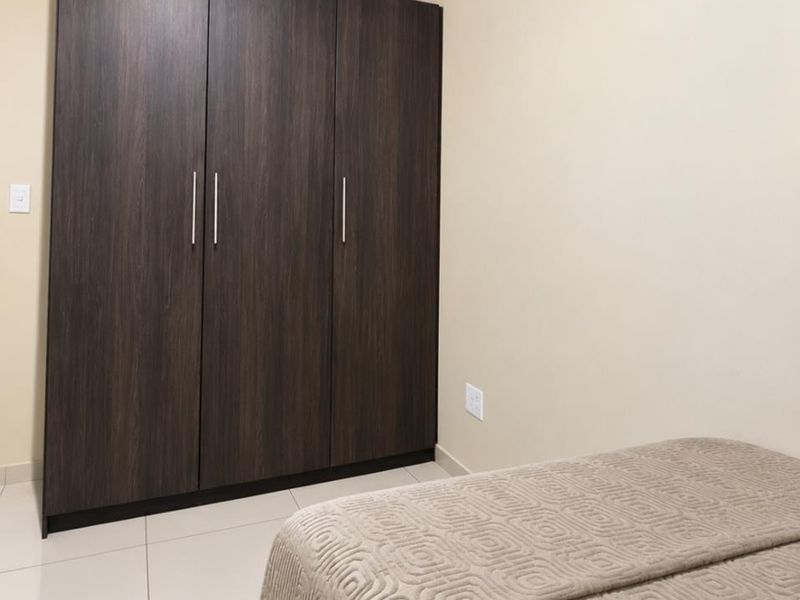 A clean bedroom featuring dark wood-finish built-in wardrobes, neutral wall paint, crown molding, and light-colored floor tiles.