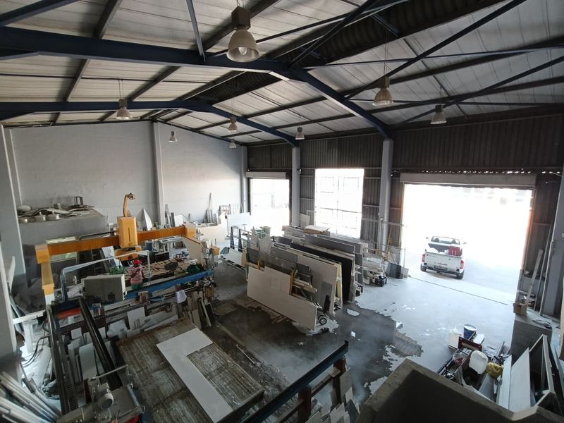 Spacious industrial warehouse featuring high ceilings with exposed steel trusses, concrete flooring, and large roller shutter doors for vehicle access.
