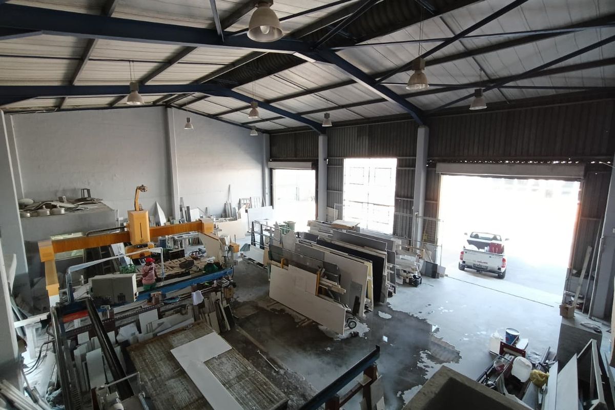 Spacious industrial warehouse featuring high ceilings with exposed steel trusses, concrete flooring, and large roller shutter doors for vehicle access.