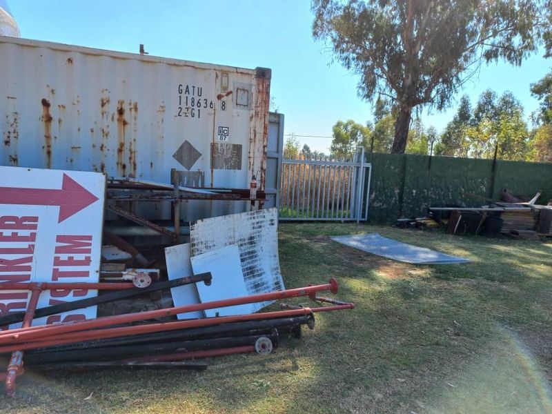 Outdoor utility area featuring a weathered shipping container, metal security gate, and perimeter fencing on the small holding property.