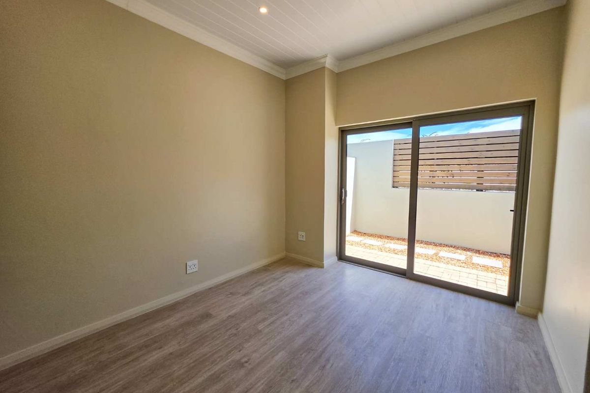 A bright, empty bedroom featuring modern laminate flooring, recessed lighting, and a sliding glass door providing direct access to a private outdoor area.