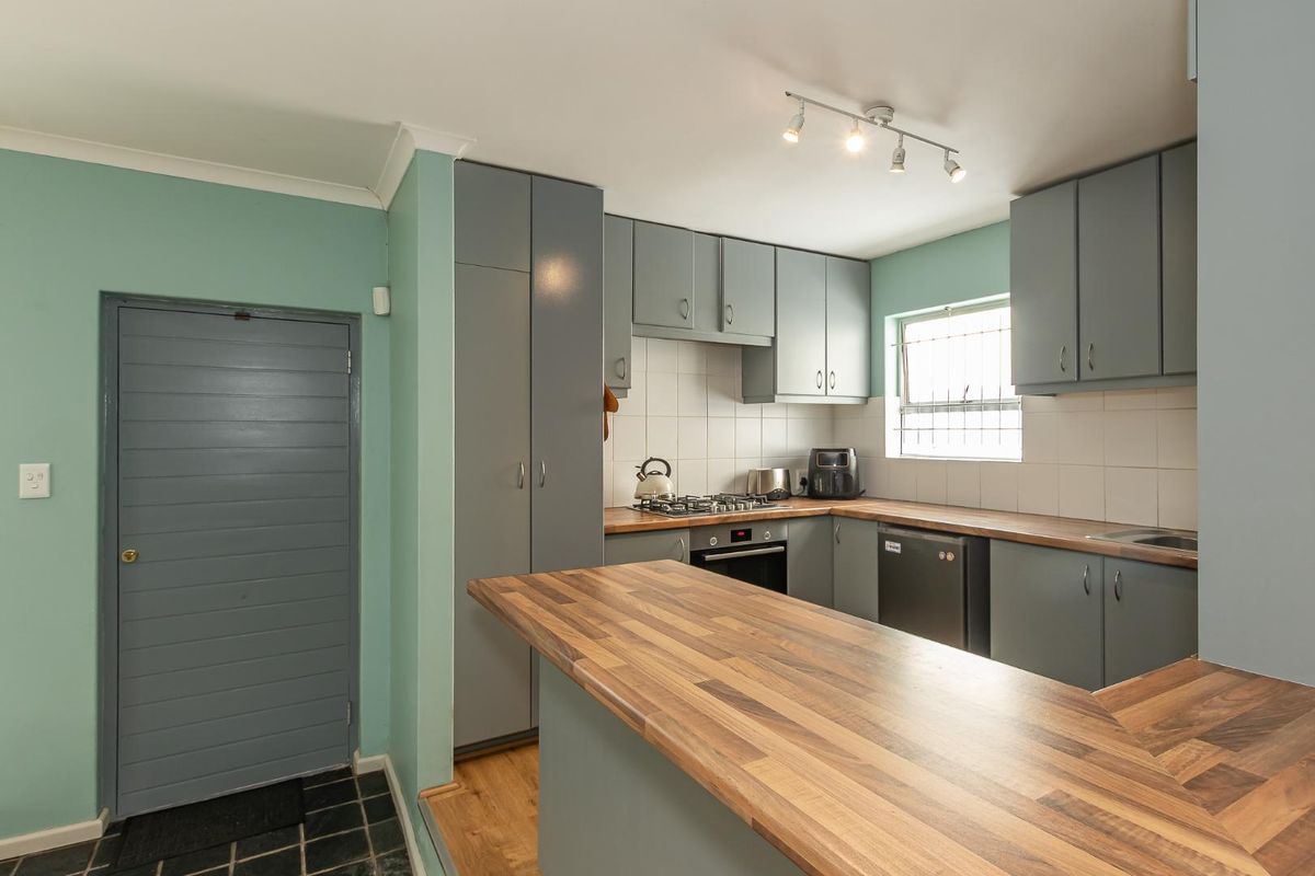 A functional kitchen featuring grey cabinetry, wood-look countertops, a built-in oven, gas hob, and tiled backsplash.