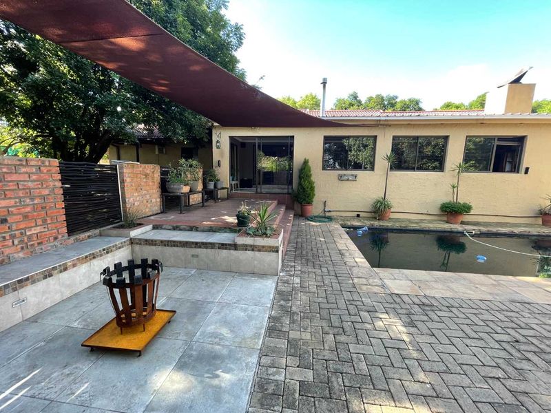 Outdoor entertainment area featuring a swimming pool, paved patio, built-in seating, and a shade sail, providing a functional space for relaxation and social gatherings.