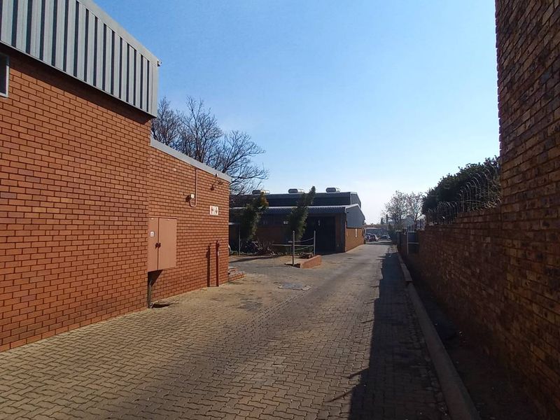 Exterior view of an industrial property featuring a paved driveway between brick buildings, with perimeter security fencing and clear access to the rear yard.