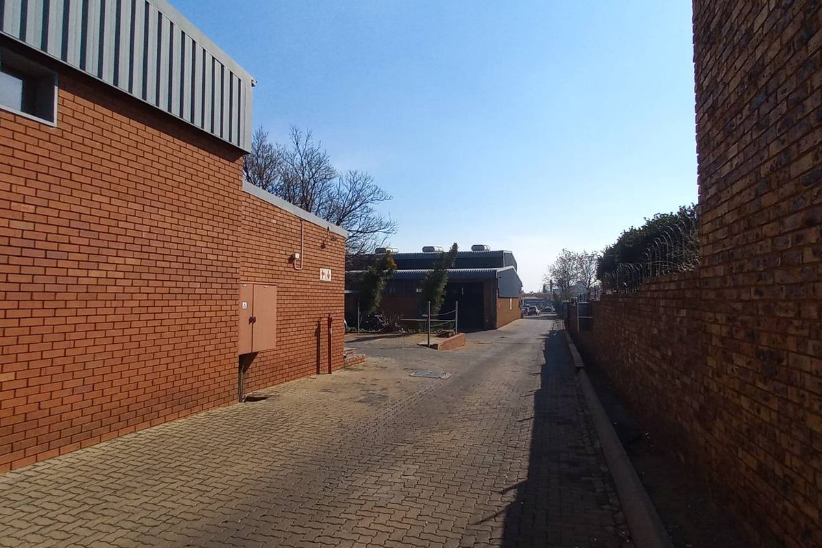 Exterior view of an industrial property featuring a paved driveway between brick buildings, with perimeter security fencing and clear access to the rear yard.