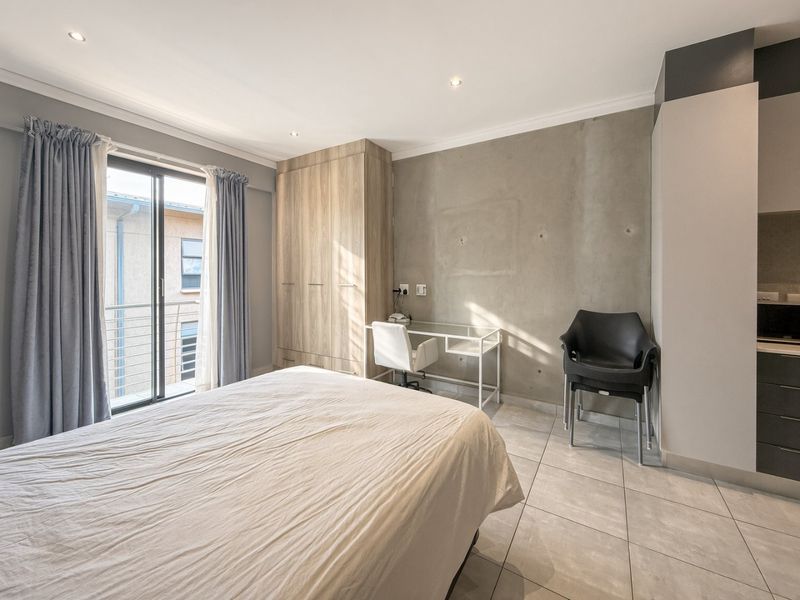 A modern bedroom featuring a concrete accent wall, built-in wooden wardrobe, tiled flooring, and a sliding glass door leading to a balcony.
