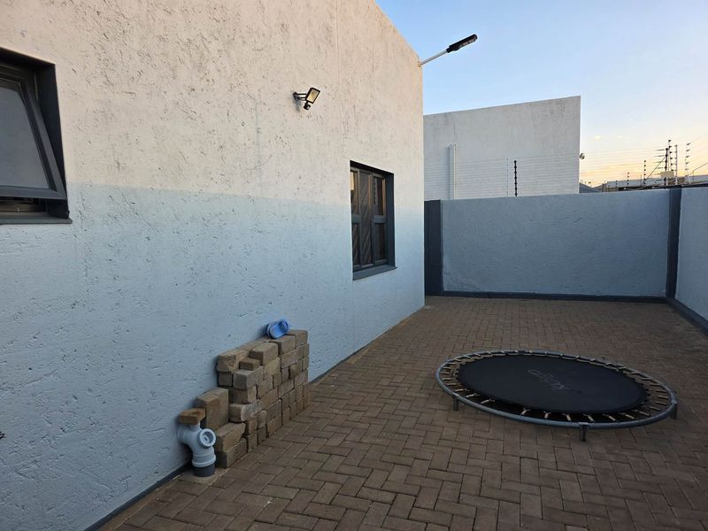 A private paved rear courtyard featuring perimeter walls with electric fencing and exterior wall-mounted lighting.