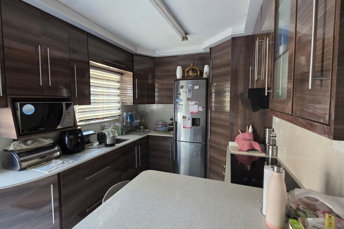 A functional kitchen featuring dark wood-grain cabinetry, stone countertops, integrated appliances, and a practical layout with ample storage space.