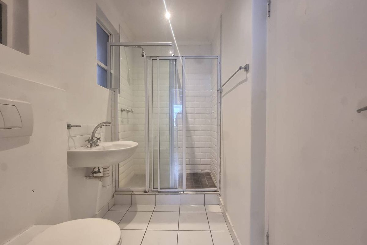 A compact, functional bathroom featuring a wall-mounted basin, a shower enclosure with subway tiling, and a concealed cistern toilet.