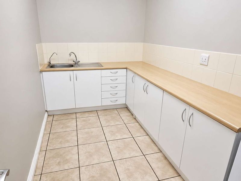 A clean and functional kitchenette featuring white cabinetry, light wood-look laminate countertops, a stainless steel sink, and neutral ceramic floor tiling.