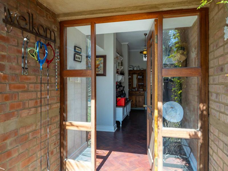 Inviting entrance featuring exposed brick walls, a classic timber-framed glass door, and warm herringbone parquet flooring leading into the home.