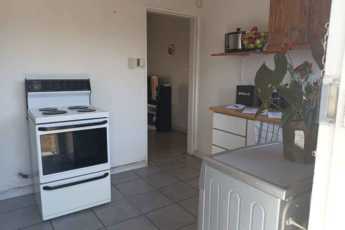 A functional kitchen area featuring tiled flooring, a freestanding stove, and wooden cabinetry, offering potential for modernization and aesthetic updates.