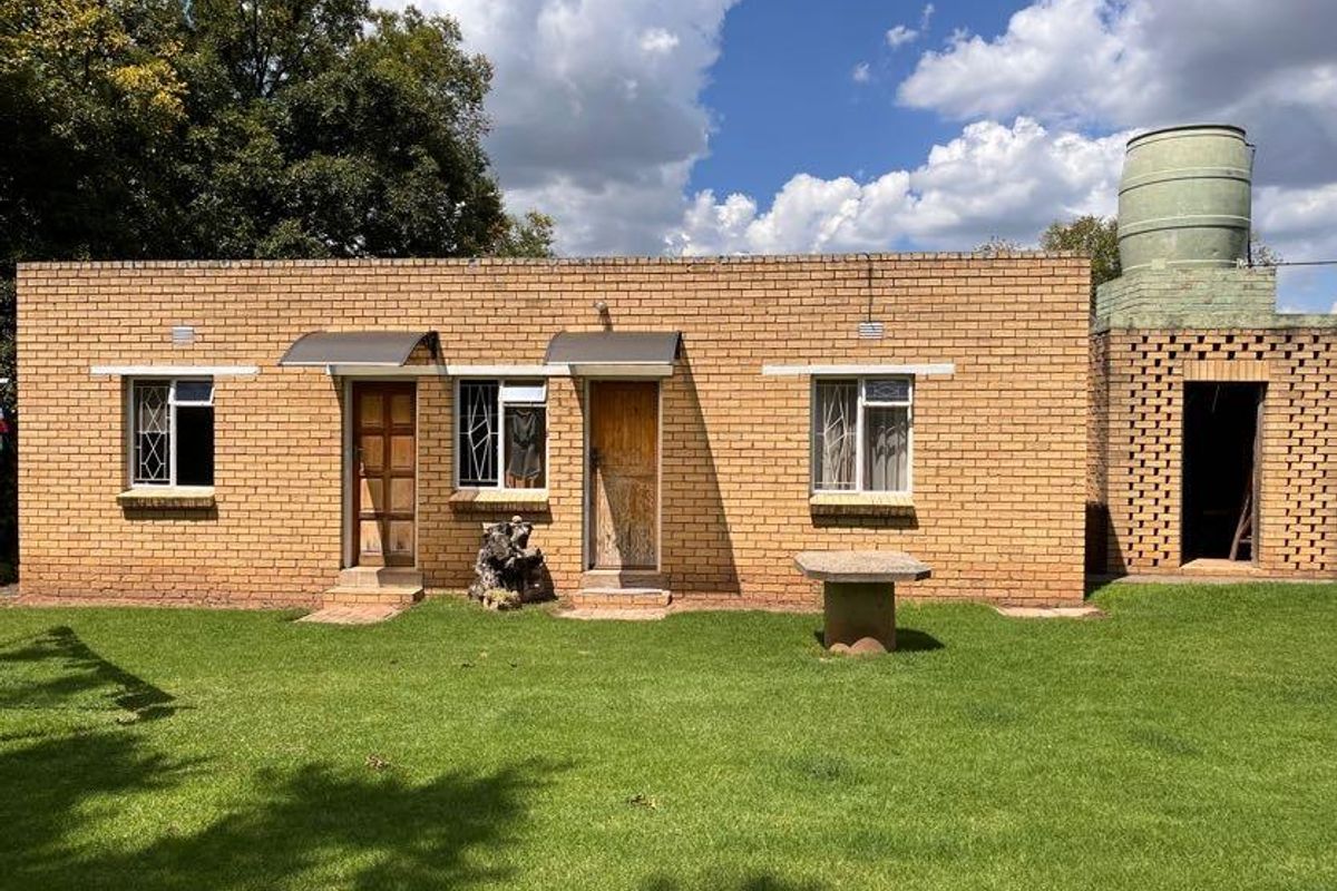 A single-story brick exterior featuring multiple entry points, security-barred windows, and an adjacent water storage tank structure set within a lawned garden.