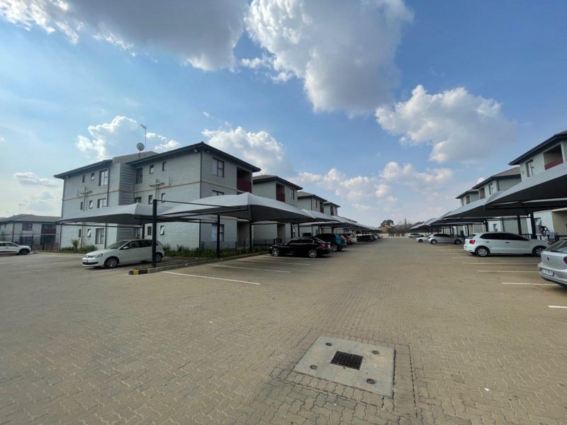 Exterior view of a residential apartment complex featuring paved parking areas with covered bays and multi-story building facades.