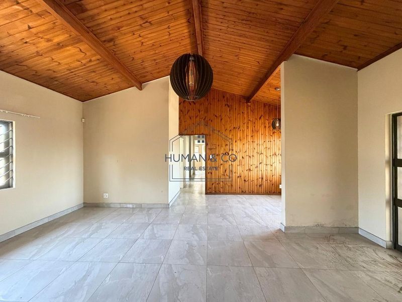 Spacious living area featuring a vaulted timber-clad ceiling, a timber feature wall, and neutral tiled flooring throughout.