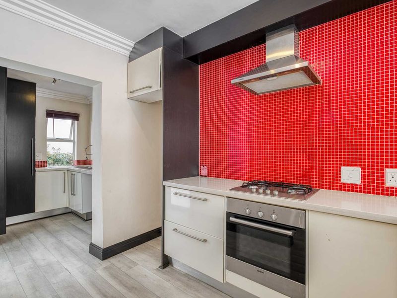 Modern kitchen featuring a bold red mosaic backsplash, built-in oven, gas hob, stainless steel extractor fan, and sleek white cabinetry with stone countertops.