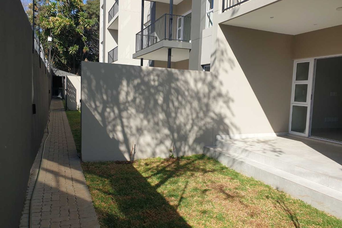 A private ground floor patio area with paved walkway, small garden space, and direct access to the apartment interior through sliding glass doors.