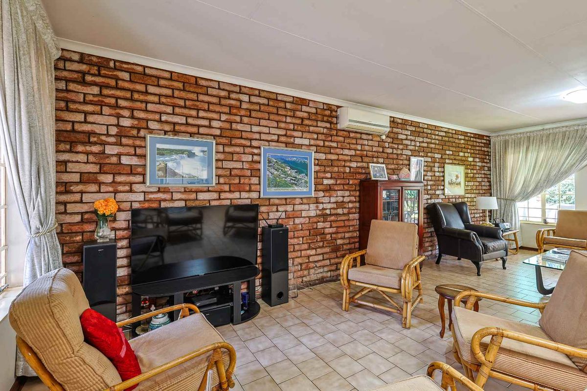 Spacious living room featuring a prominent exposed brick feature wall, tiled flooring, and a wall-mounted air conditioning unit.