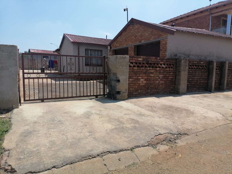 Front exterior view of the property featuring a concrete driveway, brick boundary wall, and metal security gate leading to the garage area.