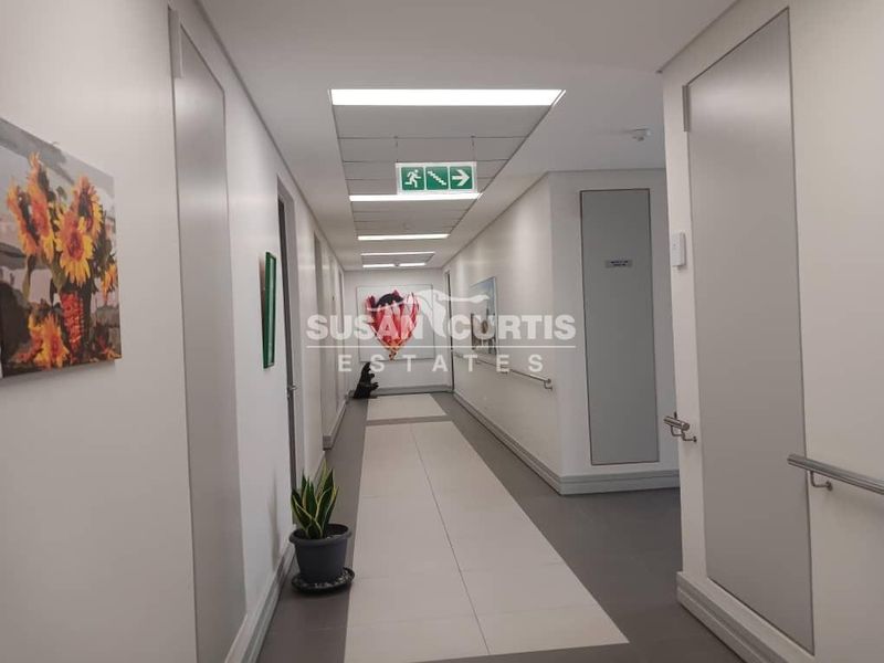 A well-maintained retirement village hallway featuring neutral tiled flooring, recessed lighting, and wall-mounted grab rails for accessibility.