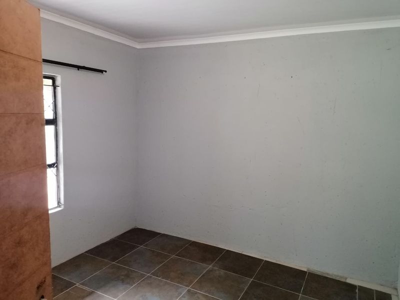 An empty bedroom featuring tiled flooring and a window with security bars, ready for a fresh coat of paint and new interior styling.