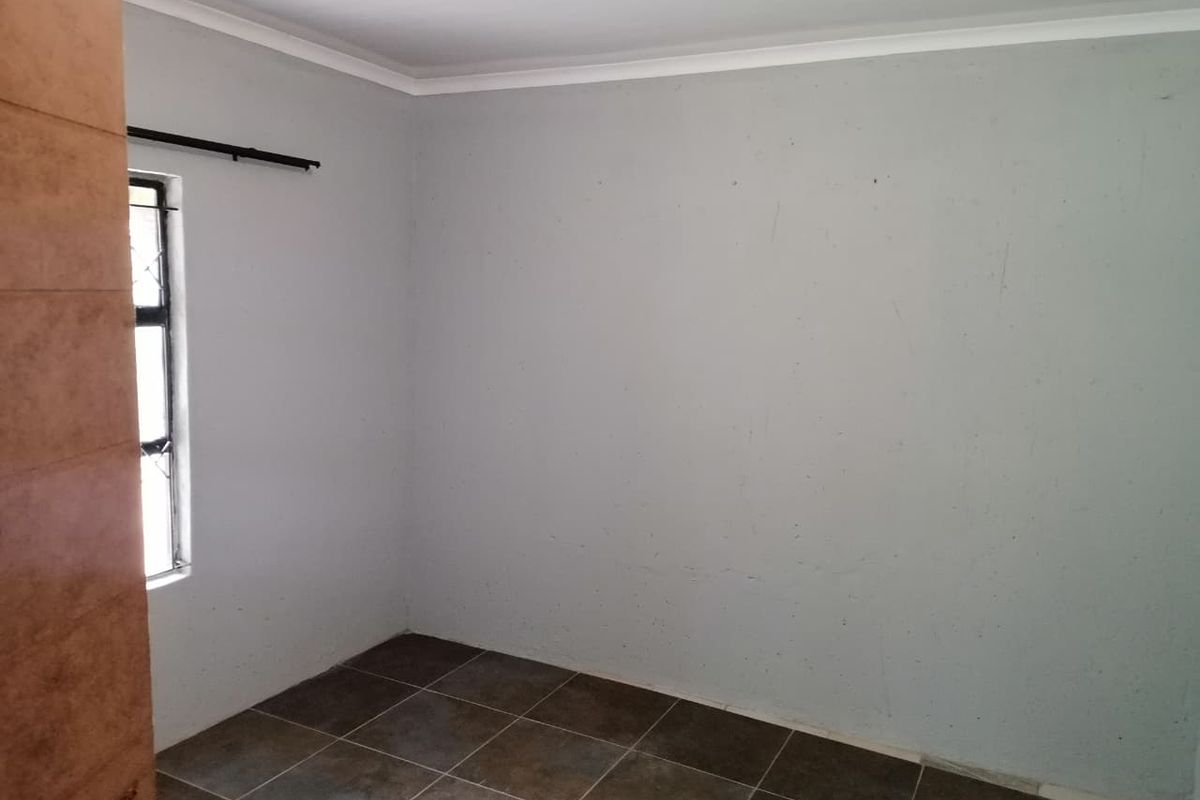 An empty bedroom featuring tiled flooring and a window with security bars, ready for a fresh coat of paint and new interior styling.