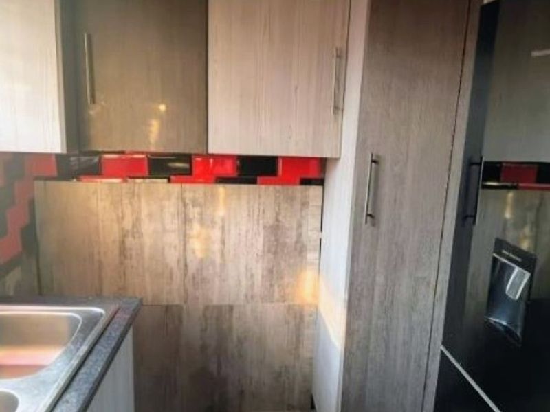 A compact kitchen area featuring wood-look cabinetry, a stainless steel sink, and a bold red and black tiled backsplash.