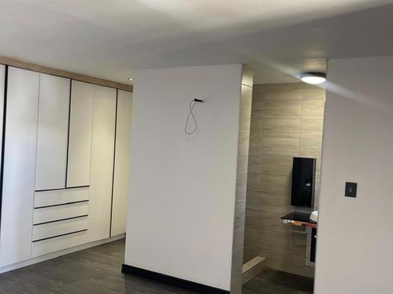 A modern bedroom featuring built-in cupboards, laminate flooring, and an open-plan ensuite area with tiled finishes.