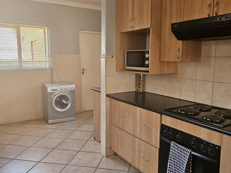 Functional kitchen featuring wood-finish cabinetry, black granite countertops, integrated oven and hob, and tiled flooring with an adjacent laundry area.