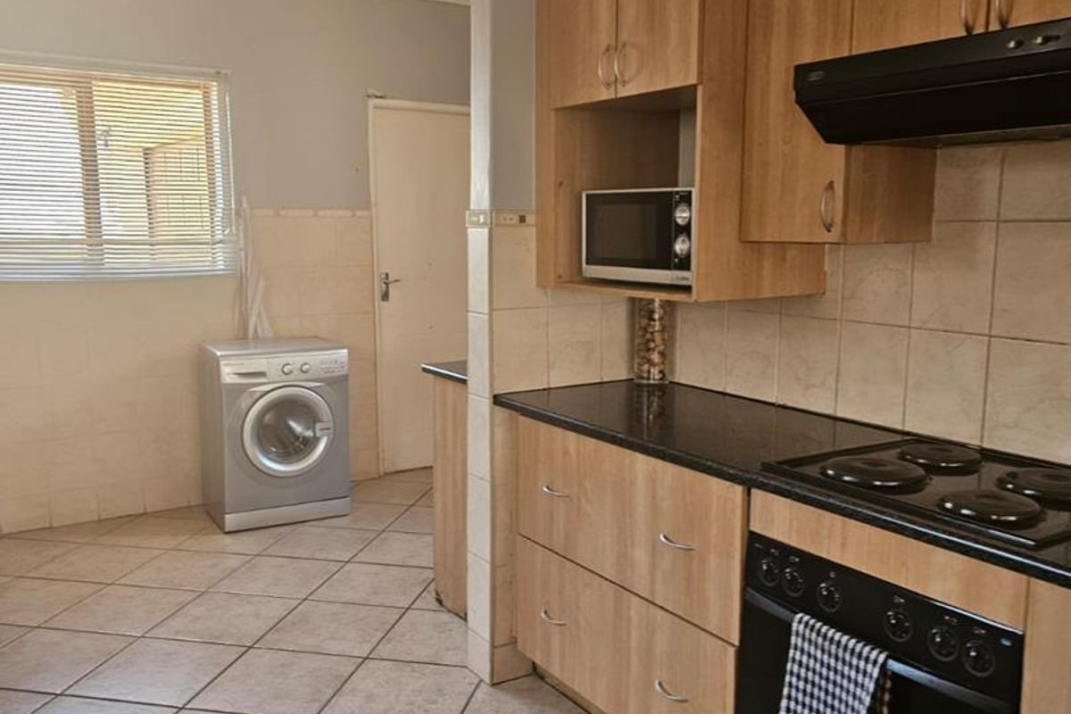 Functional kitchen featuring wood-finish cabinetry, black granite countertops, integrated oven and hob, and tiled flooring with an adjacent laundry area.