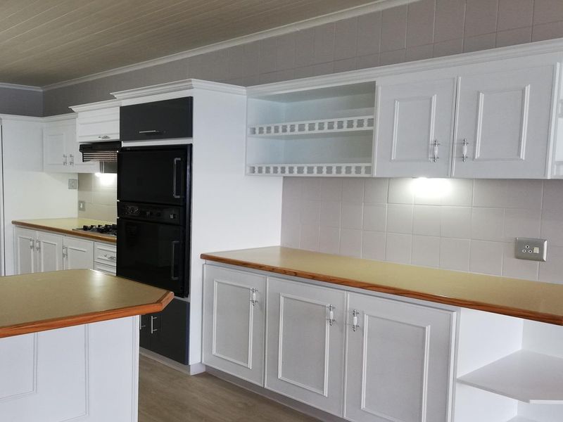 A clean, well-maintained kitchen featuring white cabinetry, laminate countertops, a built-in double oven, gas hob, and integrated extractor fan with tiled backsplash.