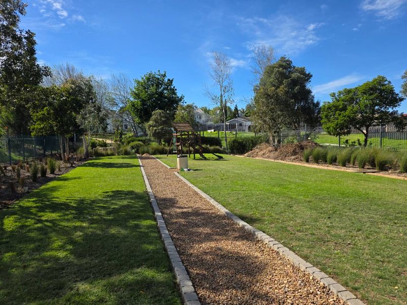 A well-maintained communal garden area featuring a central gravel pathway with brick edging, manicured lawn, and secure perimeter fencing.