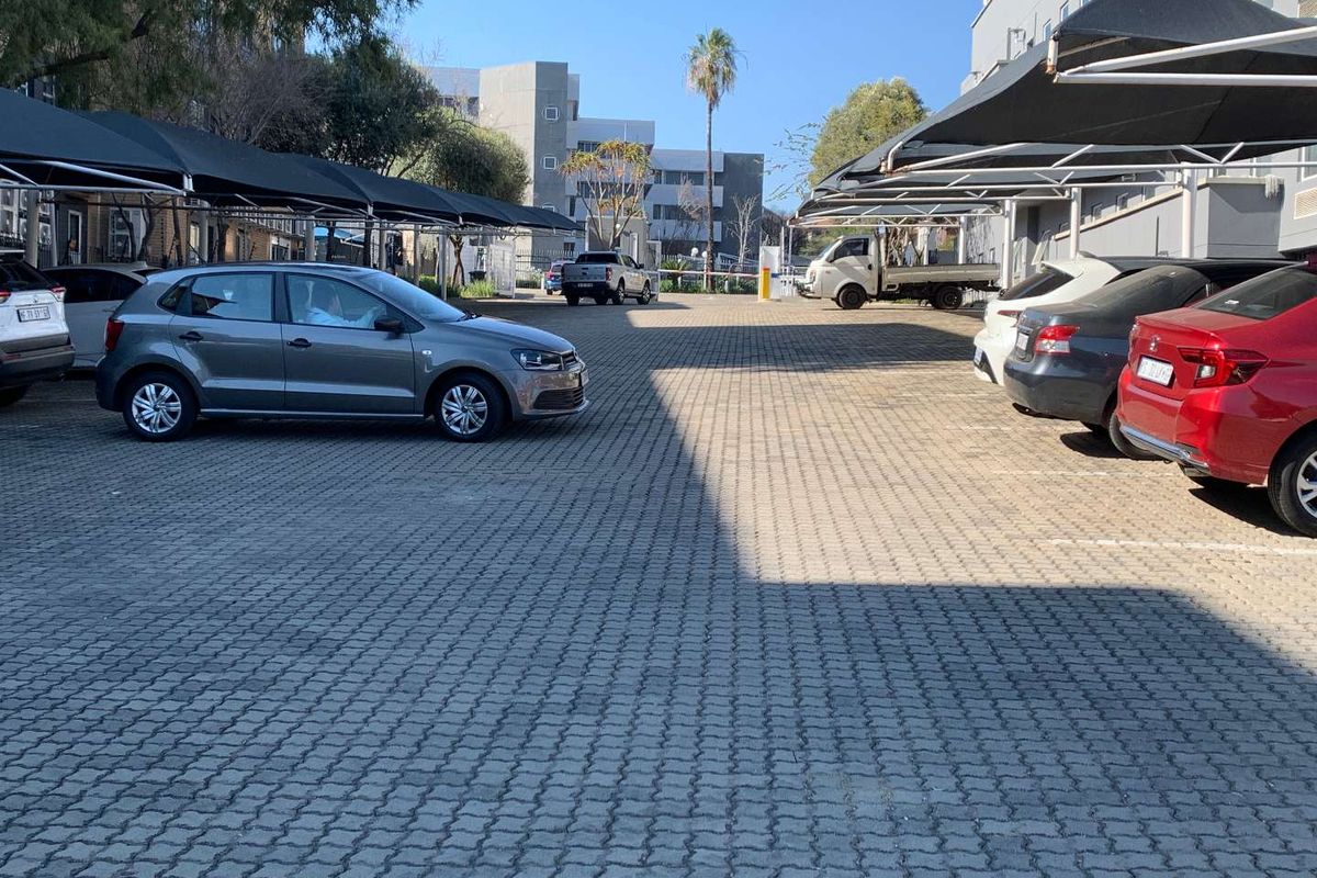 Outdoor parking area featuring paved ground and overhead shade cloth structures for vehicle protection.