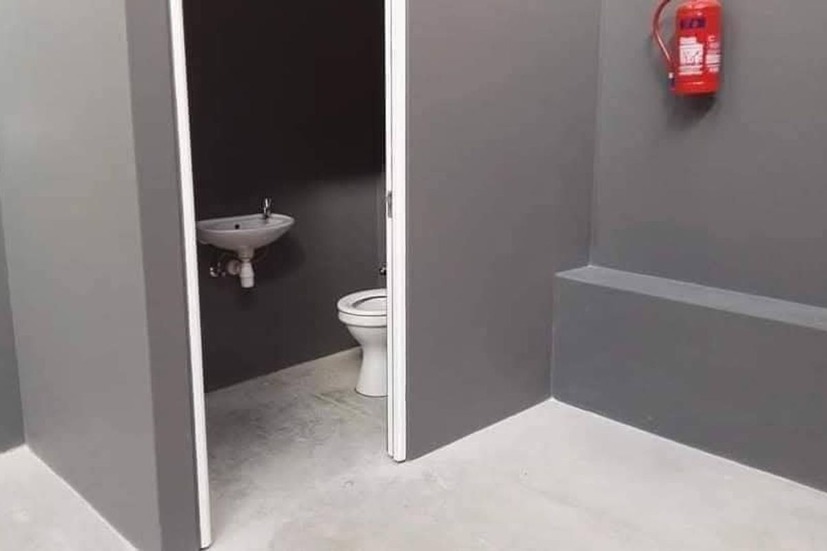 A clean, minimalist industrial-style bathroom featuring a wall-mounted basin, toilet, and a wall-mounted fire extinguisher in a neutral grey finish.