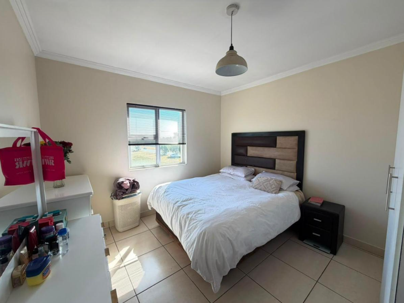 A functional bedroom featuring tiled flooring, a window with fitted blinds, and a central pendant light fixture.