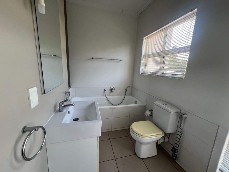 A functional bathroom featuring a built-in bathtub, vanity basin, and toilet, finished with neutral wall tiles and floor tiling.