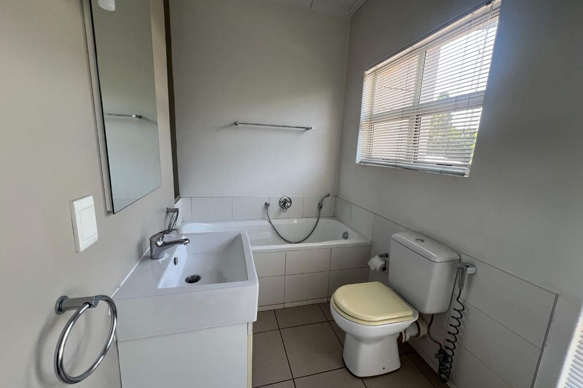 A functional bathroom featuring a built-in bathtub, vanity basin, and toilet, finished with neutral wall tiles and floor tiling.