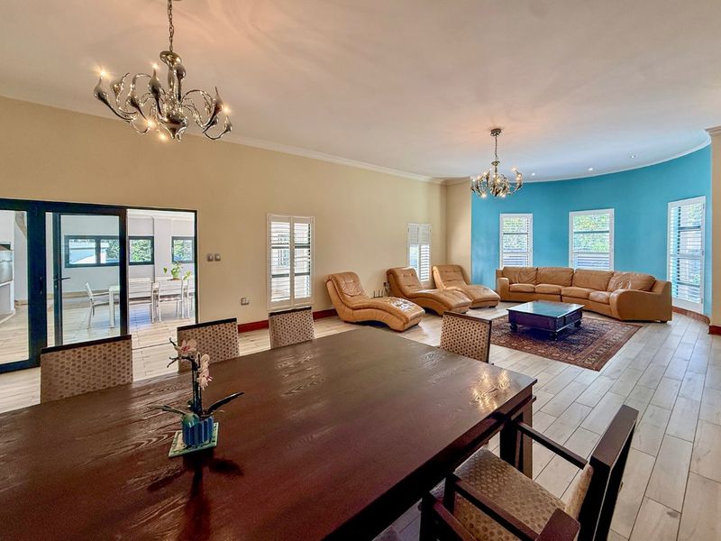 Spacious open-plan living and dining area featuring tiled flooring, decorative chandeliers, and plantation shutters, with seamless access to an adjoining patio space.