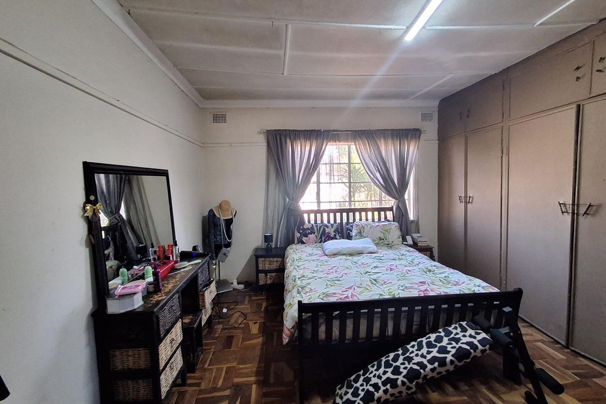 A bedroom featuring parquet flooring, built-in cupboards, and a window with security bars. The room requires cosmetic updates to the ceiling and flooring.