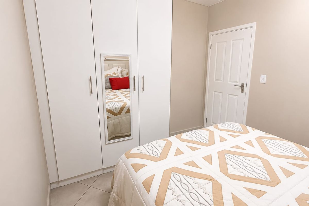 A well-maintained bedroom featuring neutral wall tones, tiled flooring, and a functional built-in wardrobe with a mirrored panel.