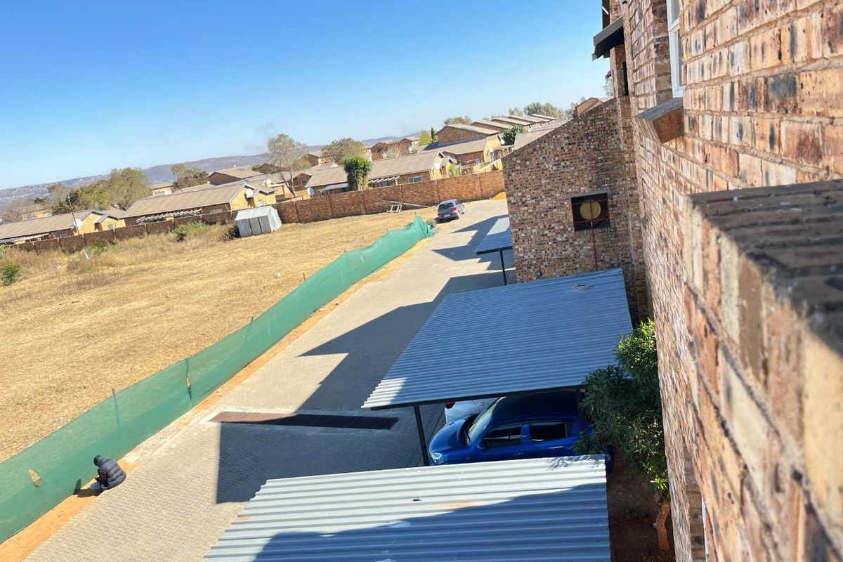 Elevated view of the apartment complex exterior, featuring face brick architecture, paved driveway, and corrugated metal carports.
